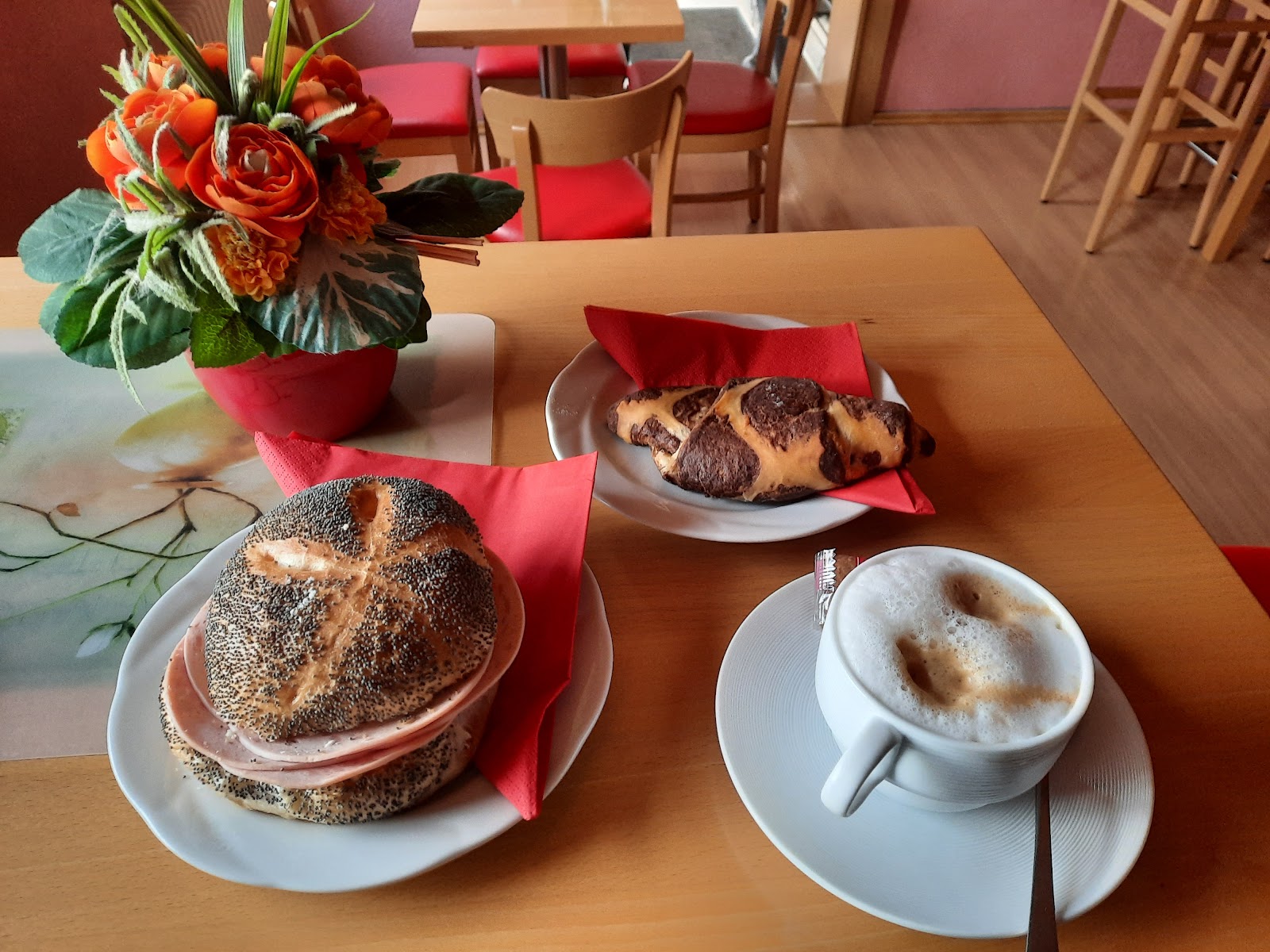 Mohnbrötchen, Croissant und Cappuccino mit Blumenstrauß